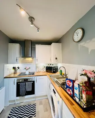 a kitchen with white cabinets and a clock on the wall at Luxurious & Modern Apartment in Hawkhead