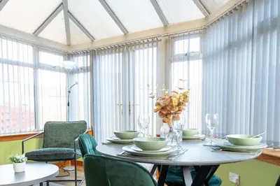 a dining room with a table and chairs and windows at Gunn House in Grangemouth
