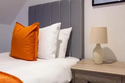 a bed with an orange pillow and a lamp on a table at Winton House in Glasgow