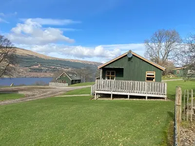 a green house on a field next to a lake at Bracken Lodges, Loch Tay, Linnie Lodge in Aberfeldy