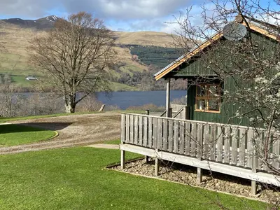 a green building with a bench next to a lake at Bracken Lodges, Loch Tay, Linnie Lodge in Aberfeldy