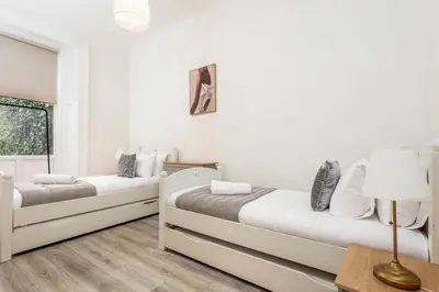 two beds in a white room with a lamp at Cuthbert House in Prestwick