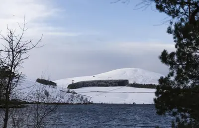 a mountain covered in snow next to a body of water at Shepherds Cottage, Pentland Hills in Nine Mile Burn
