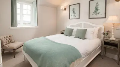 a bedroom with a white bed and a chair and a window at The Coach House, Pentland Hills in Nine Mile Burn