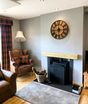 a living room with a fireplace and a clock on the wall at Clarinnes Cottage in Luss