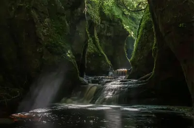 a waterfall in a cave in a forest at The Mar Huts - The Lomond Hut in Drymen