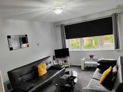 a living room with a black leather couch and yellow pillows at PREMIER - Maryhill Apartment in Glasgow
