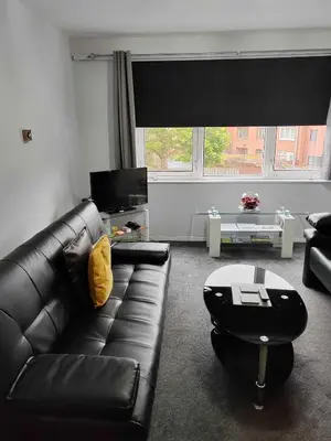 a living room with a black leather couch and a table at PREMIER - Maryhill Apartment in Glasgow