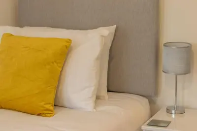a white bed with a yellow pillow and a lamp at 2 bed flat near airport &parking in Paisley
