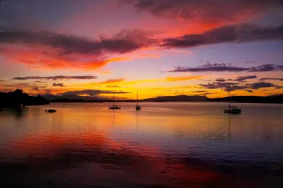 a sunset with boats on a body of water at Appin Holiday Homes -Caravans, Lodges, Shepherds Hut and Train Carriage stays in Appin
