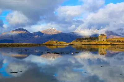 a castle on an island in a body of water with mountains at Appin Holiday Homes -Caravans, Lodges, Shepherds Hut and Train Carriage stays in Appin