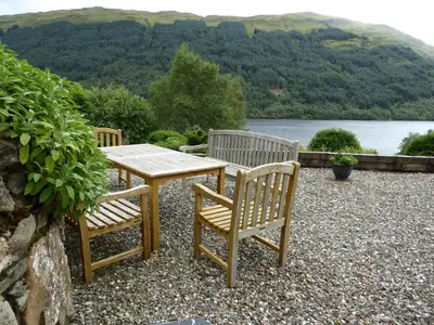 a wooden table and two chairs sitting next to a lake at Craigruie Farmhouse in Balquhidder