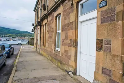 a dog sitting next to a white door on a brick building at 6 Killean Place in Campbeltown