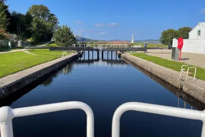 a boat in a canal with a bridge in the background at Janeville Holiday Apartment in Ardrishaig
