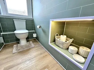 a bathroom with a toilet in a green tiled wall at Newly Renovated Gem - Free Parking & Modern Comfort in Glasgow