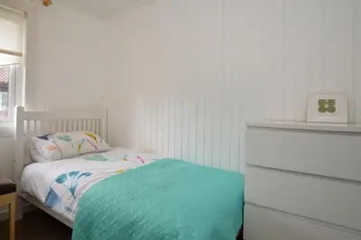 a white bedroom with a bed with a blue blanket at Harris's Cabin in Hunters Quay