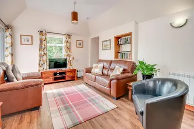 a living room with leather furniture and a tv at Courtyard Cottages, Garden Cottage in Wigtown