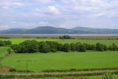 a green field with trees and mountains in the background at Courtyard Cottages, Garden Cottage in Wigtown