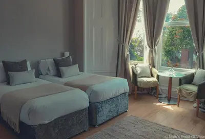 a bedroom with two beds and a table and a window at Hotel Baba in Uddingston