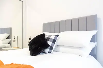 a bed with a black and white pillow on it at 1 BDR Apartment By Caledonia Luxe Stays Short Lets & Serviced Accommodation in Dumbarton