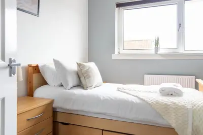 a bedroom with a bed with white sheets and a window at Blairmuire House in Broxburn