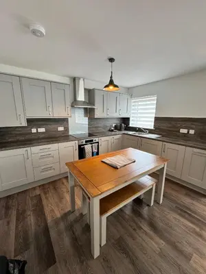 a kitchen with white cabinets and a wooden table at Inchmoan Apartment in Bonhill