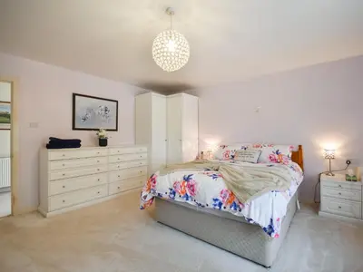 a white bedroom with a bed and two dressers at Nether Auchlinsky Cottage in Glendevon