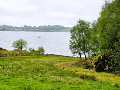 a boat on the water with a field and trees at Ard Veich Estate - Panoramic Highland Sea Views with private beach and woodland in Port Appin