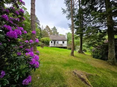 a house in the middle of a yard with purple flowers at Ard Veich Estate - Panoramic Highland Sea Views with private beach and woodland in Port Appin