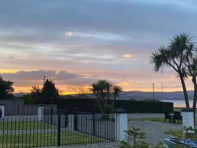 a fence with palm trees and a sunset in the background at 2 bed Lodge near Dunoon on the Shore Front in Dunoon
