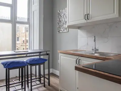 a kitchen with white cabinets and a sink and stools at West End Cosy Pop of Colour - Pass the Keys in Glasgow