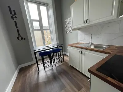 a kitchen with white cabinets and a sink and stools at West End Cosy Pop of Colour - Pass the Keys in Glasgow