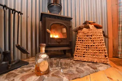 a bottle of whiskey and glasses on a table with a stove at Rowan Log Cabin in Dalavich
