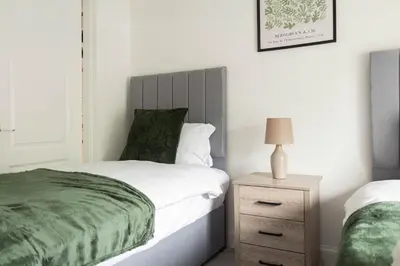 a bedroom with a bed and a nightstand with a green blanket at 3 BDR House At Caledonia Luxe Stays Short Lets & Serviced Accommodation Tillicoultry in Tillicoultry