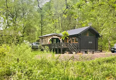 a cabin in the middle of a forest with a car at Seil Log Cabin in Dalavich