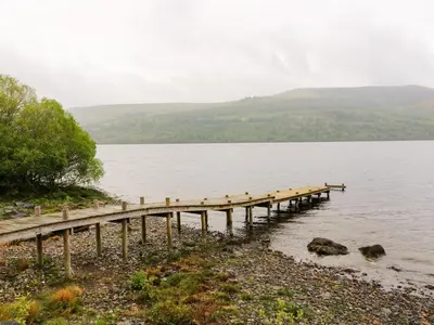 a dock on a lake with hills in the background at Kalipé in Aberfeldy