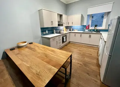 a kitchen with white cabinets and a wooden table at Beautiful spacious apartment in town centre in Oban