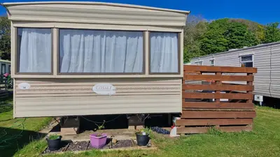 a tiny house in a yard next to a fence at Static Caravan situated at Wigbay, Stranraer in Stranraer