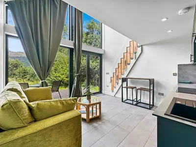 a living room with a couch and large windows at Aos Sí - Wellness - Jacuzzi - Lodges in Ballachulish