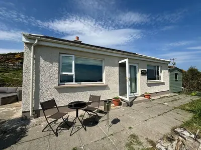 a house with two chairs and a table in front of it at Stunning Rathlin cottage in Rathlin Island