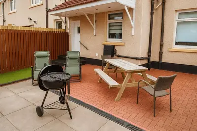 a patio with a wooden table and chairs and a table and a table at Register House Family or Contractor 4bed with Garden Driveway in Bellshill