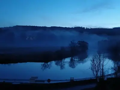 a misty lake with trees in the middle at Idyllic Waterside Penthouse in Callander