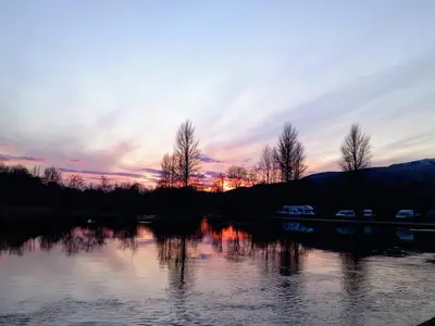 a sunset over a body of water with trees at Idyllic Waterside Penthouse in Callander
