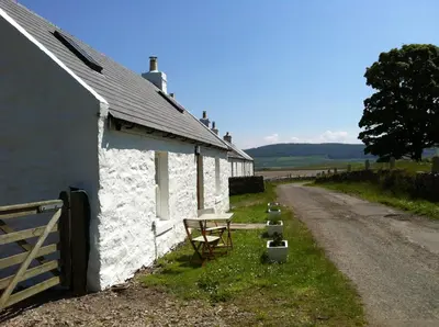a white building with a fence next to a road at Cnocachanach Cottage in Tarbert