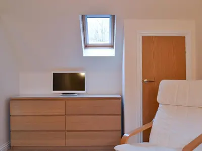 a room with a television on a dresser with a chair at Pine Marten Cottage in Ballachulish