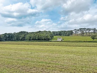 a large field with a white house on a hill at Balnowlart Lodge in Ballantrae