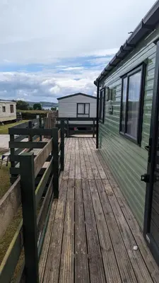 a large wooden deck next to a green trailer at The Brockenhurst 25 in Dunoon
