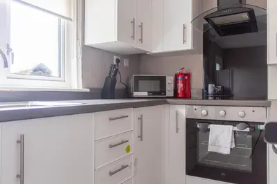 a kitchen with white cabinets and a stove and a microwave at Campsie View in Glasgow