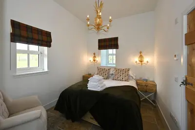 a bedroom with a bed with a chair and a chandelier at The Bothy in Buchanty