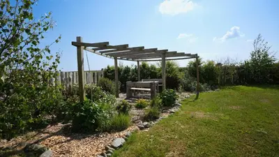 a wooden pergola with a bench in a garden at The Galloway Steading - The Fox's Den with Hot Tub and Fire Pit in Glenluce